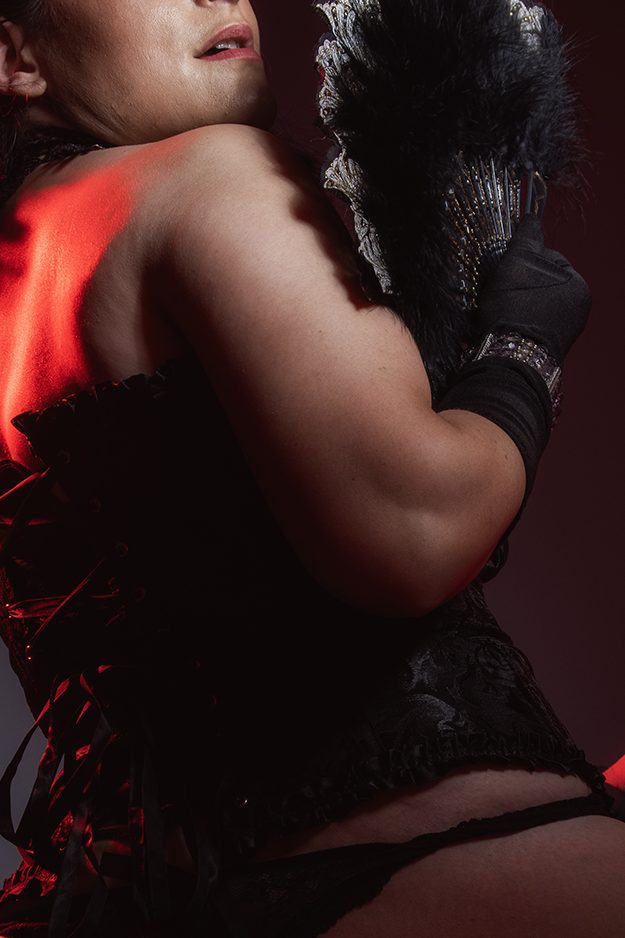 Burlesque, woman photographed in low light holding a fan

