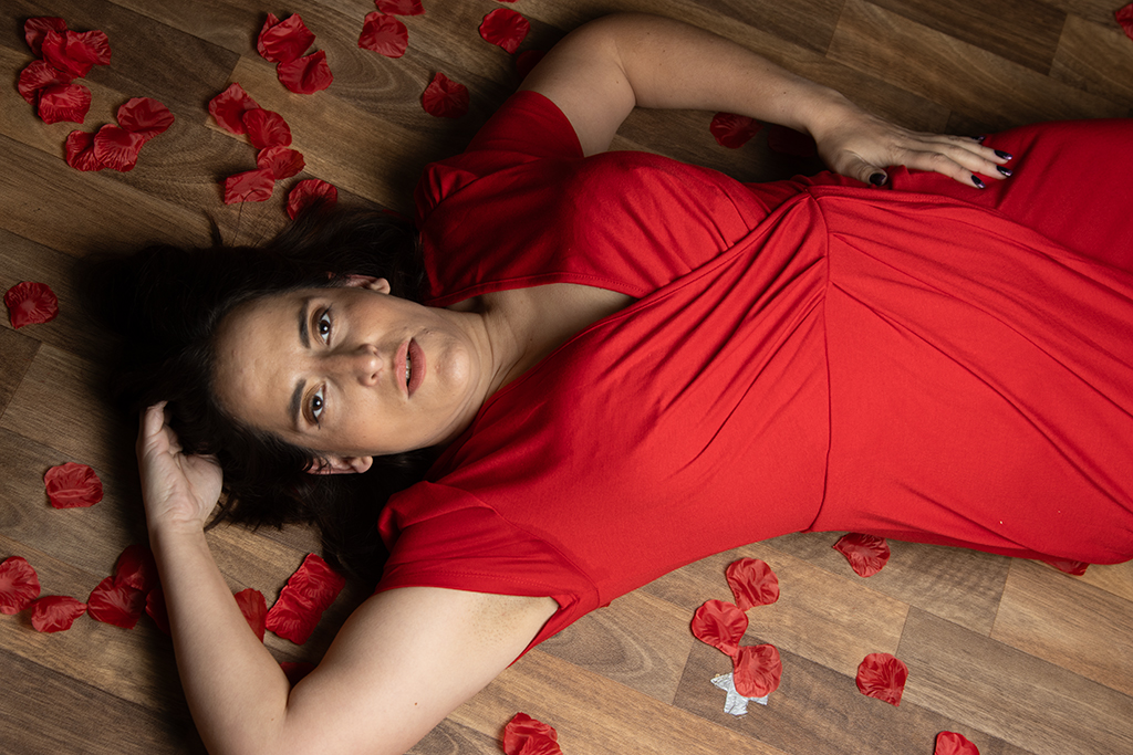 brunette in red dress, lying down surrounded by rose petals